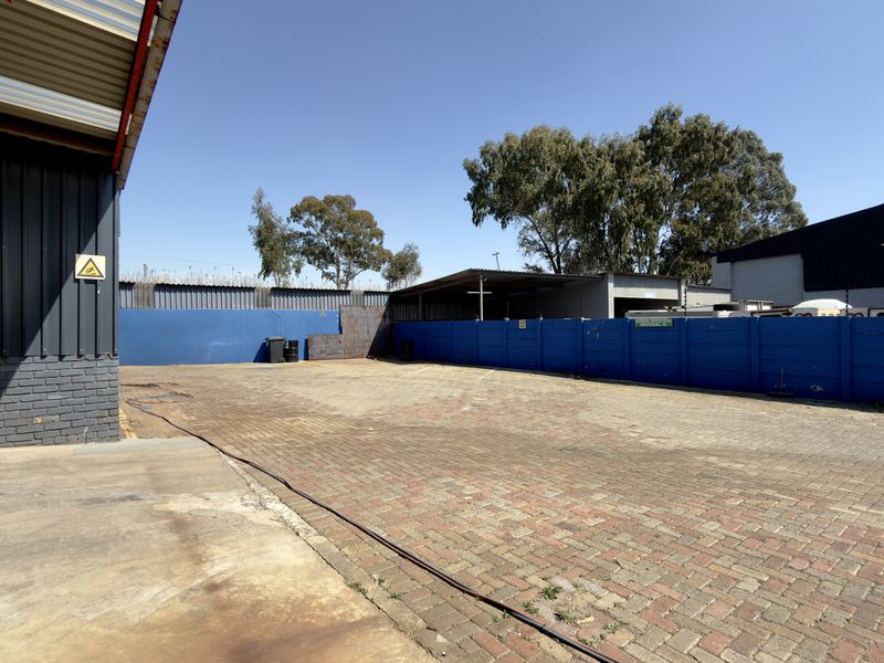 A spacious commercial paved yard area featuring a designated wash bay, enclosed by perimeter walls and adjacent to industrial metal-clad structures.