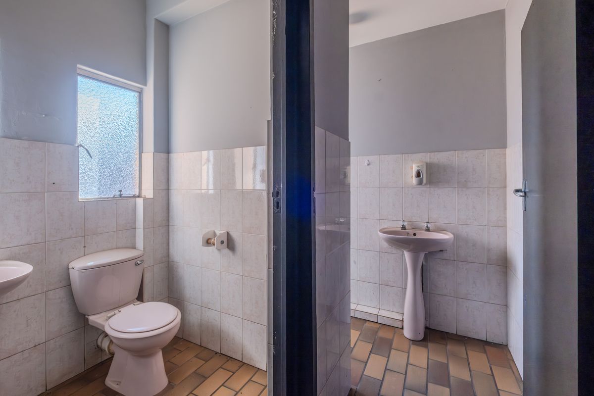 A functional office restroom featuring a pedestal basin, toilet, and tiled finishes, providing essential facilities for a professional workspace.