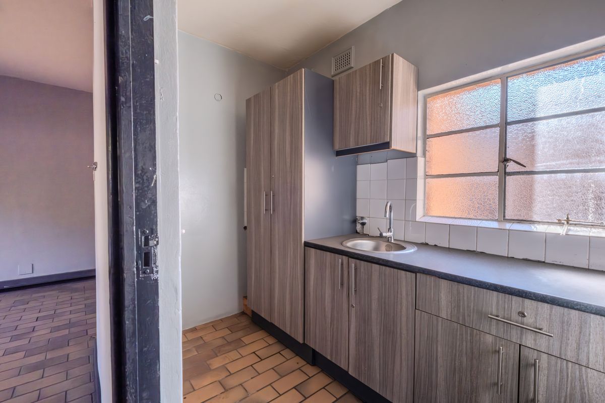 A functional kitchenette area featuring wood-grain cabinetry, a stainless steel sink, tiled backsplash, and a window providing natural light.
