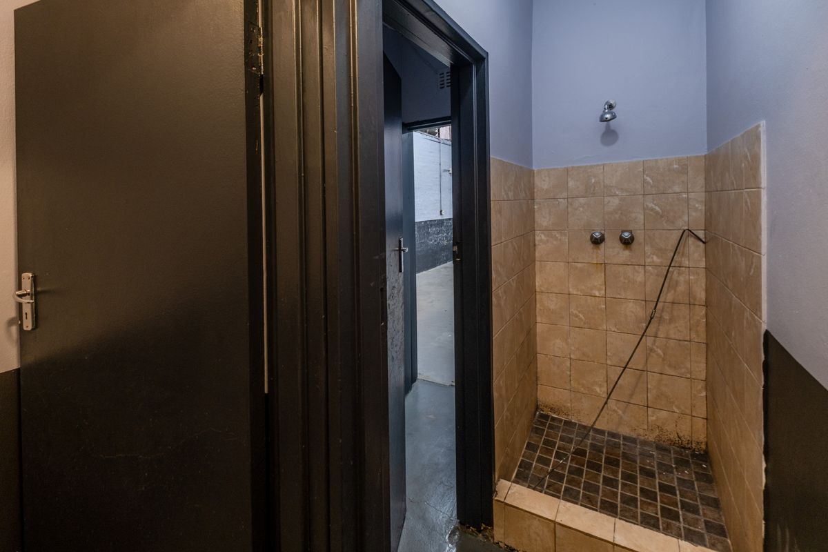 A functional industrial shower area featuring tiled walls, a raised shower base, and direct access to an adjacent utility space.