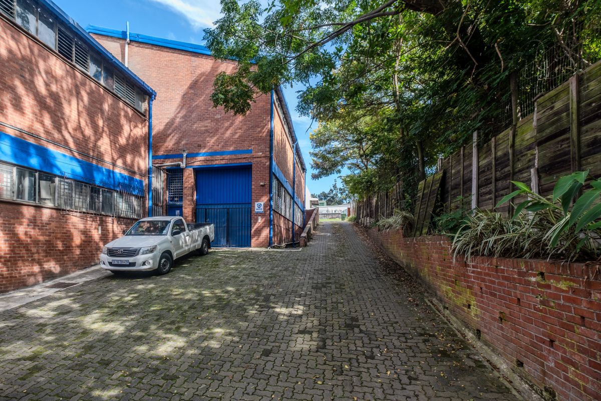 Industrial property exterior featuring a paved driveway, brick facade, and secure metal roller door access.
