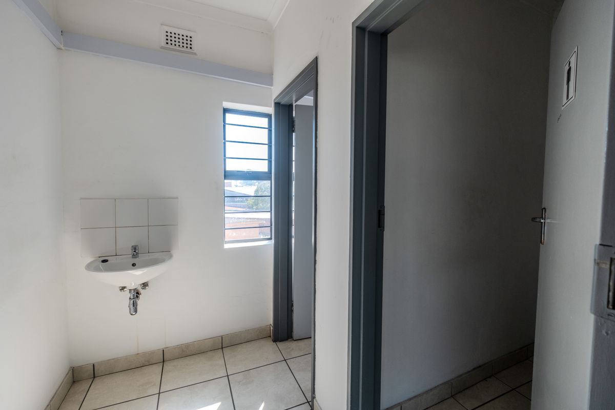 A functional industrial restroom area featuring a wall-mounted basin, tiled flooring, and secure window access.