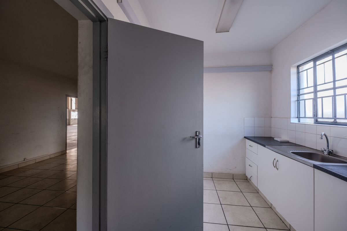 A functional kitchenette area featuring white cabinetry, a dark countertop, stainless steel sink, and tiled flooring, with an adjacent open-plan space visible.