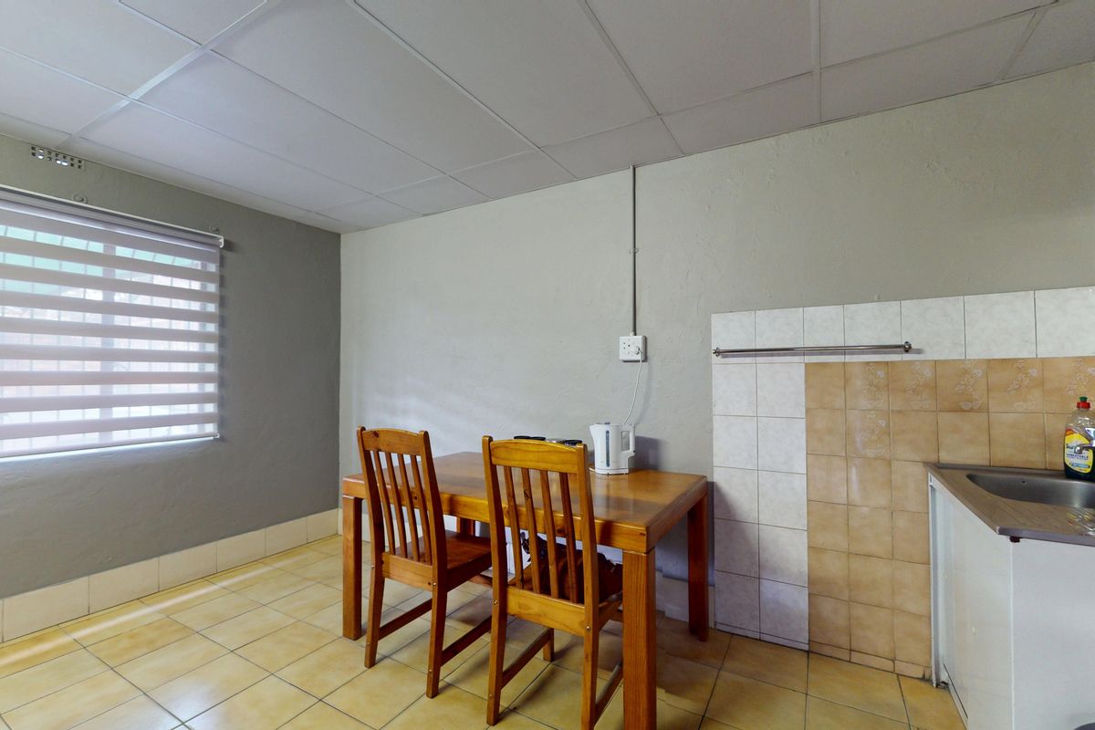 A functional kitchen area featuring tiled flooring, a basic sink unit, and tiled splashbacks, with exposed electrical wiring and a drop ceiling.