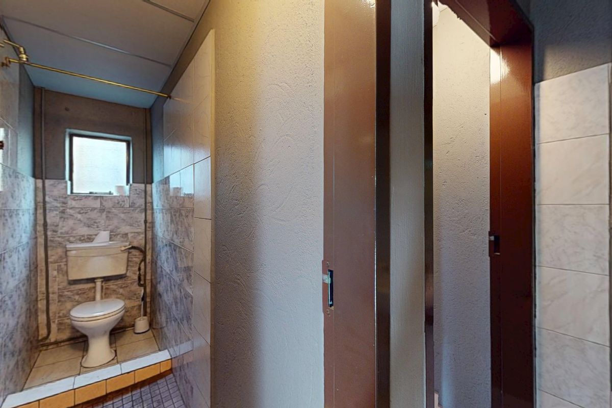 A functional bathroom featuring a standard toilet, tiled walls, and exposed plumbing fixtures, showing signs of age and wear.