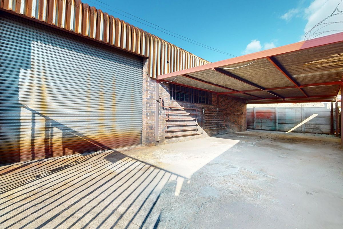 Industrial exterior space featuring a large roller shutter door, covered parking area, and durable brick construction suitable for storage or workshop use.
