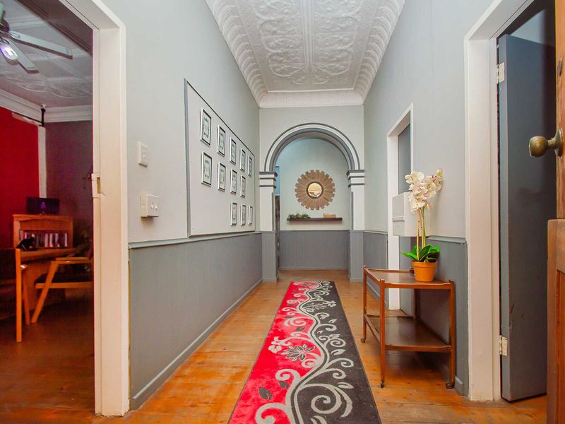 A character-filled hallway featuring original pressed metal ceilings, timber flooring, and classic wainscoting, leading through an elegant archway.