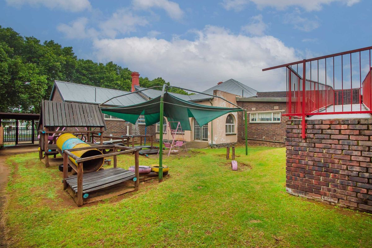 Rear exterior view of a commercial property featuring a brick facade, metal roofing, and an outdoor play area with a shade structure.