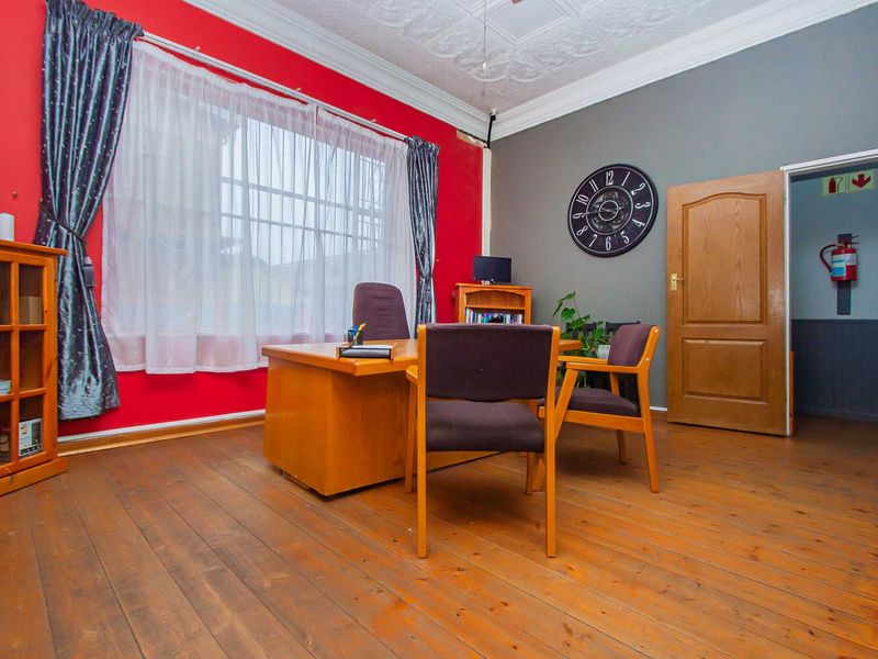 A functional office space featuring original timber flooring, ornate ceiling detailing, and a large window with security bars.