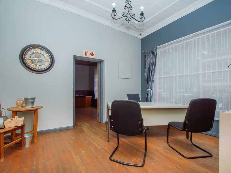 A functional office space featuring original timber flooring, high ceilings with decorative molding, and large windows with security bars.