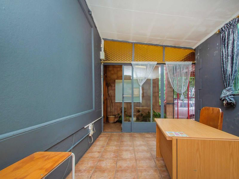 A functional office space featuring tiled flooring, a sliding glass door entrance, and dark-toned walls, suitable for a professional workspace or commercial reception area.