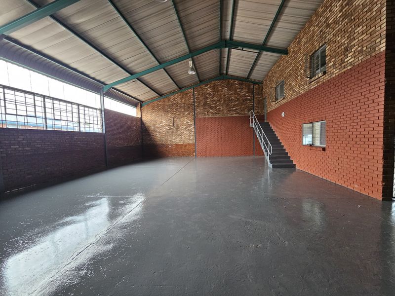 Spacious industrial warehouse unit featuring exposed brick walls, polished concrete flooring, high-clearance steel roof trusses, and an internal metal staircase.