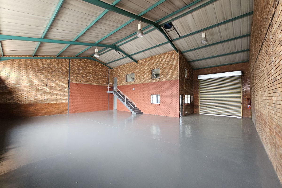 Spacious industrial warehouse unit featuring exposed brick walls, painted concrete flooring, high-clearance steel roof trusses, and a large roller shutter door for easy access.
