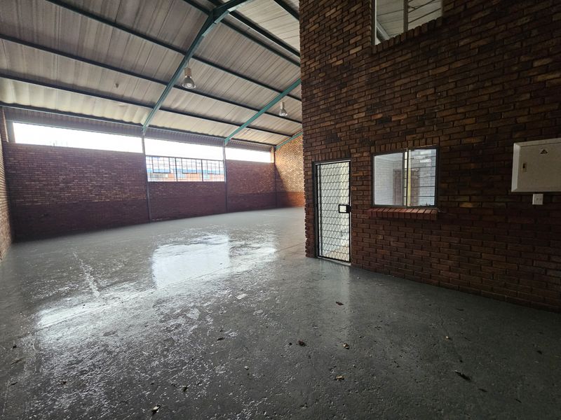 Spacious industrial utility area featuring exposed brickwork, high steel truss ceilings, and durable epoxy-coated concrete flooring with an integrated office or storage enclosure.