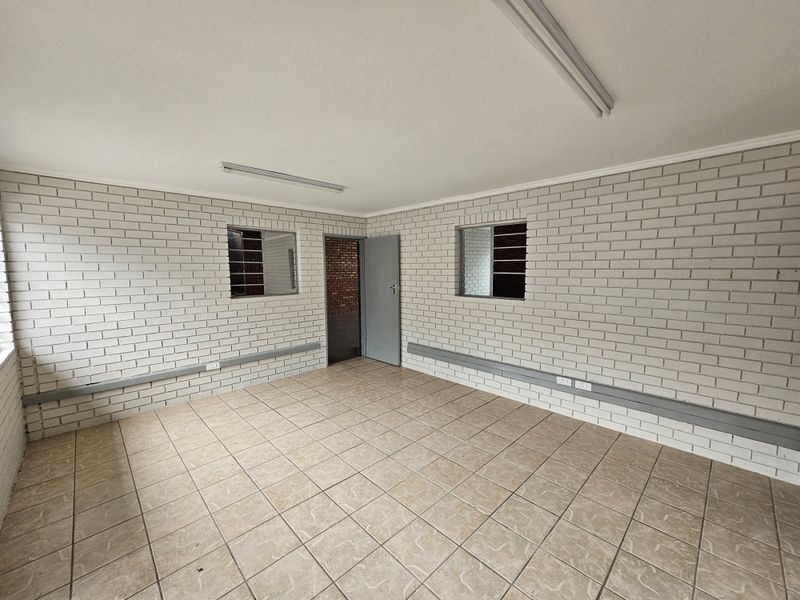 A clean, empty industrial office space featuring painted brick walls, ceramic tile flooring, and functional fluorescent lighting.