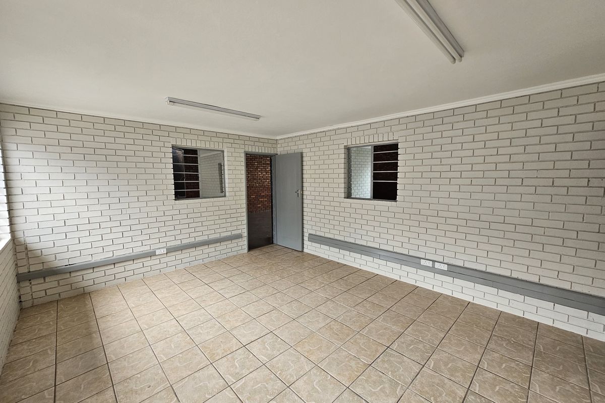 A clean, empty industrial office space featuring painted brick walls, ceramic tile flooring, and functional fluorescent lighting.