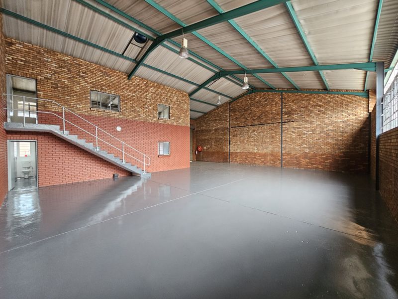 Spacious industrial warehouse unit featuring exposed brick walls, polished epoxy flooring, a steel staircase, and high-clearance metal roof structure.
