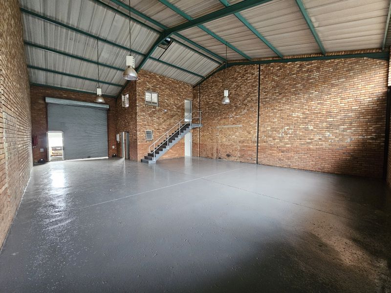 Spacious industrial warehouse unit featuring exposed brick walls, high ceilings with steel trusses, polished epoxy flooring, and a large roller shutter door.