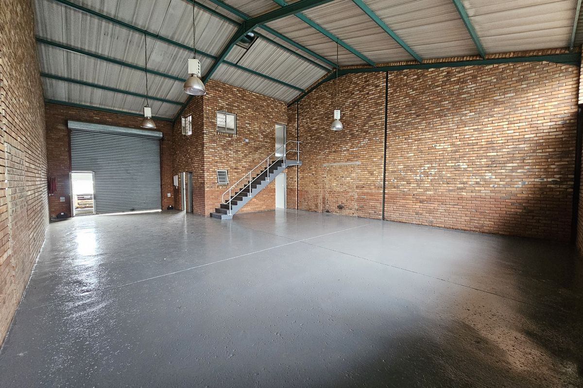Spacious industrial warehouse unit featuring exposed brick walls, high ceilings with steel trusses, polished epoxy flooring, and a large roller shutter door.