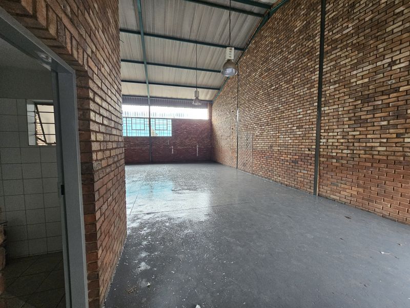 Spacious industrial utility area featuring exposed brick walls, high pitched metal roofing, and durable epoxy-coated concrete flooring, suitable for various commercial or storage uses.