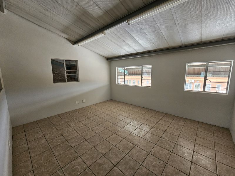 An empty, functional utility space featuring tiled flooring, exposed metal ceiling, and multiple steel-framed windows providing natural light.