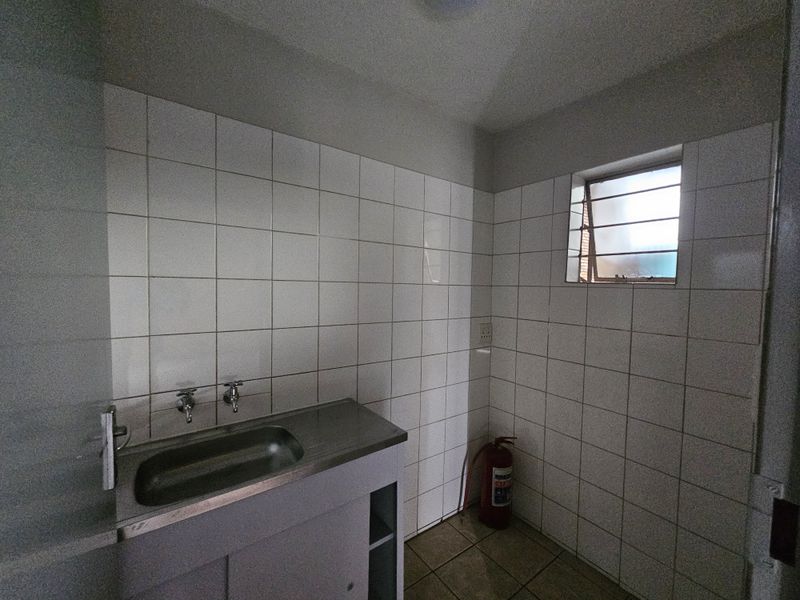 A functional laundry area featuring tiled walls, a stainless steel sink, and a louver window for ventilation.