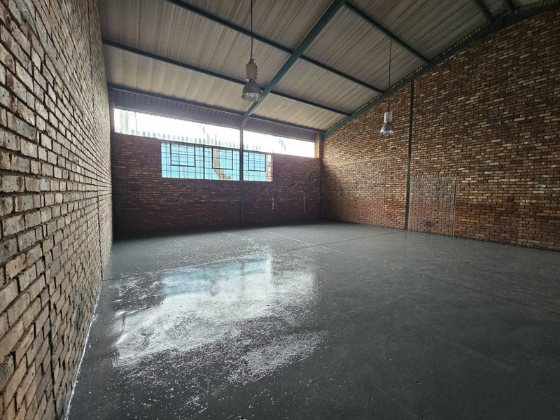 Spacious industrial utility area featuring exposed brick walls, polished concrete flooring, and high-clearance steel roof trusses with industrial pendant lighting.