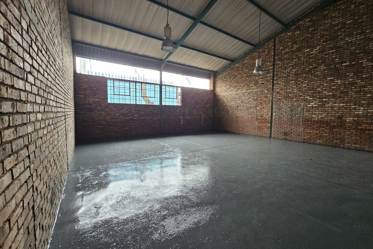 Spacious industrial utility area featuring exposed brick walls, polished concrete flooring, and high-clearance steel roof trusses with industrial pendant lighting.