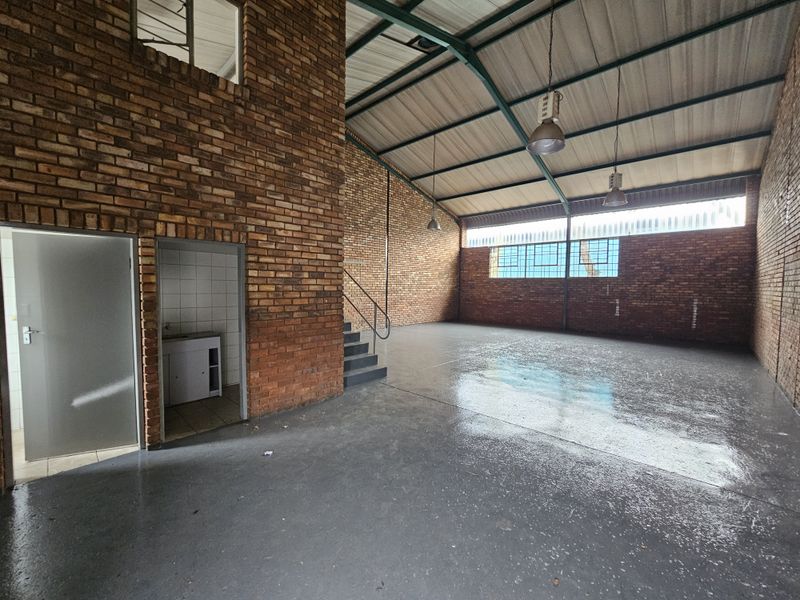 Spacious industrial warehouse unit featuring exposed brick walls, high ceilings with steel trusses, polished concrete flooring, and a small integrated kitchenette area.
