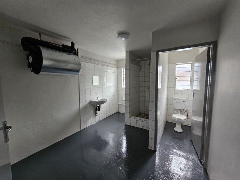 Functional industrial-style bathroom featuring a tiled shower stall, pedestal sink, toilet, and wall-mounted water heater with painted concrete flooring.