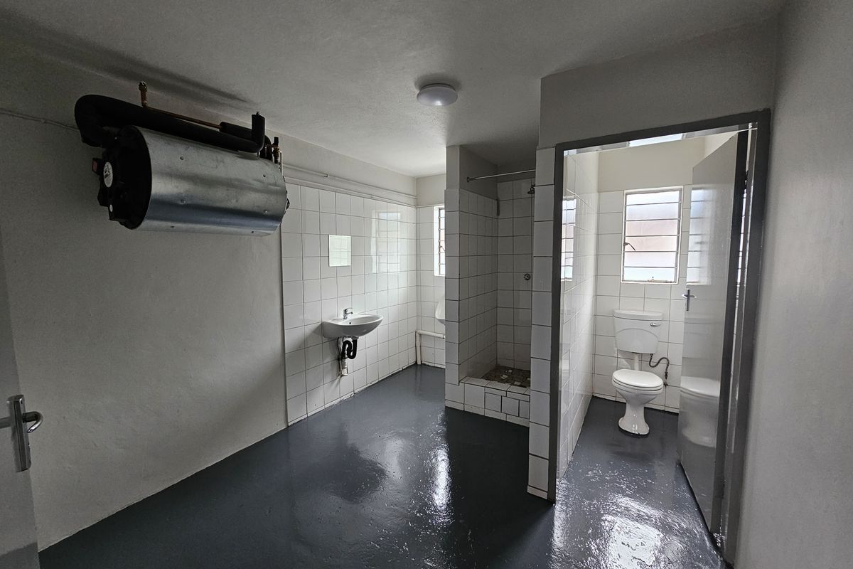 Functional industrial-style bathroom featuring a tiled shower stall, pedestal sink, toilet, and wall-mounted water heater with painted concrete flooring.