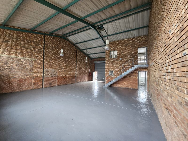 Spacious industrial warehouse unit featuring exposed brick walls, polished concrete flooring, steel staircase, and high-clearance roof with industrial lighting.
