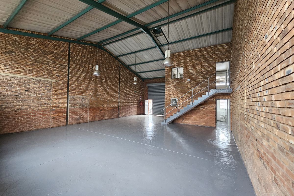 Spacious industrial warehouse unit featuring exposed brick walls, polished concrete flooring, steel staircase, and high-clearance roof with industrial lighting.