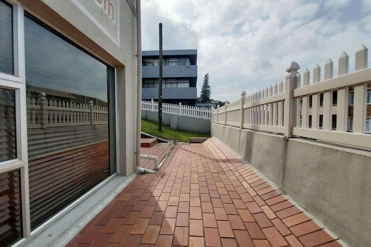 A paved exterior side walkway featuring a white picket fence, retaining wall, and large glass windows along the building facade.