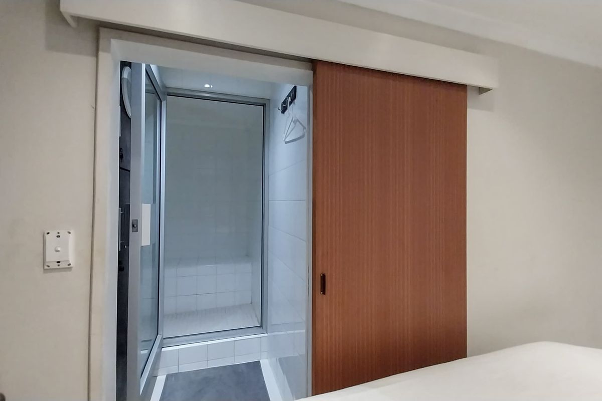 A view of a bathroom entrance featuring a sliding wooden door and a tiled shower enclosure with a built-in bench.