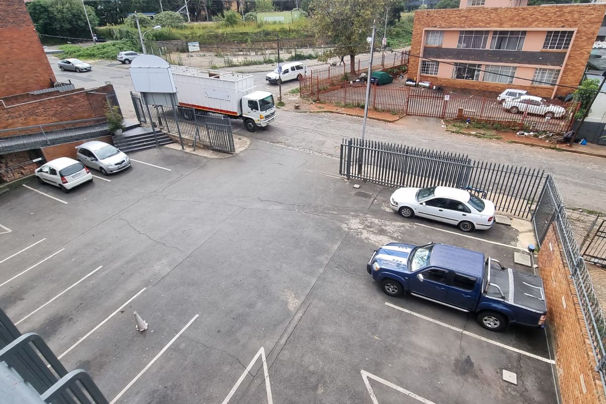 An elevated view of a commercial parking area featuring asphalt surfacing, perimeter metal fencing, and gated access to the street.