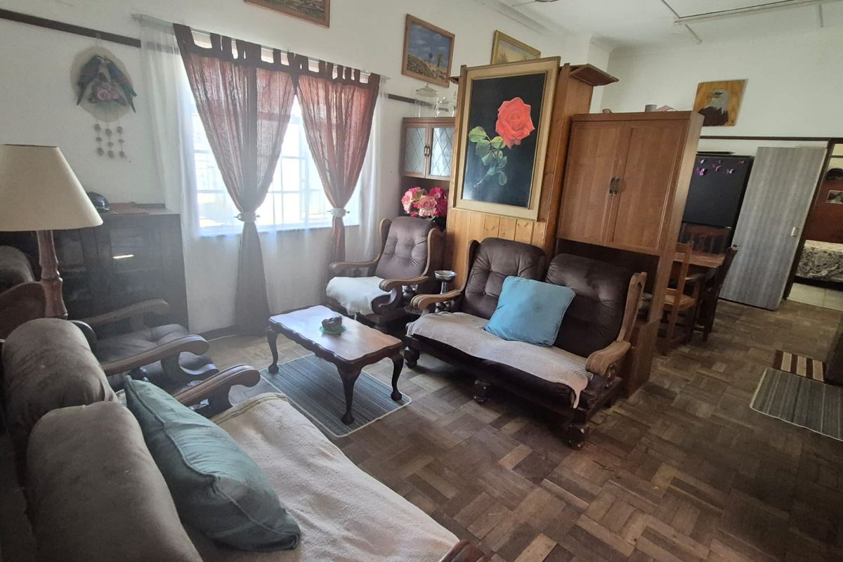 A living area featuring traditional parquet flooring, a ceiling fan, and large windows allowing natural light into the space.
