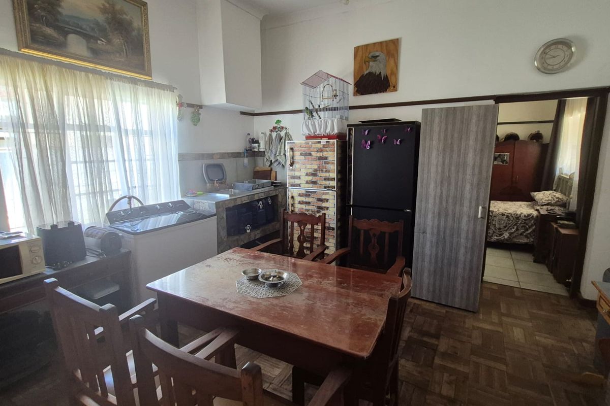 A dated kitchen and dining area featuring parquet flooring, built-in cabinetry, and a functional layout with direct access to an adjacent bedroom.