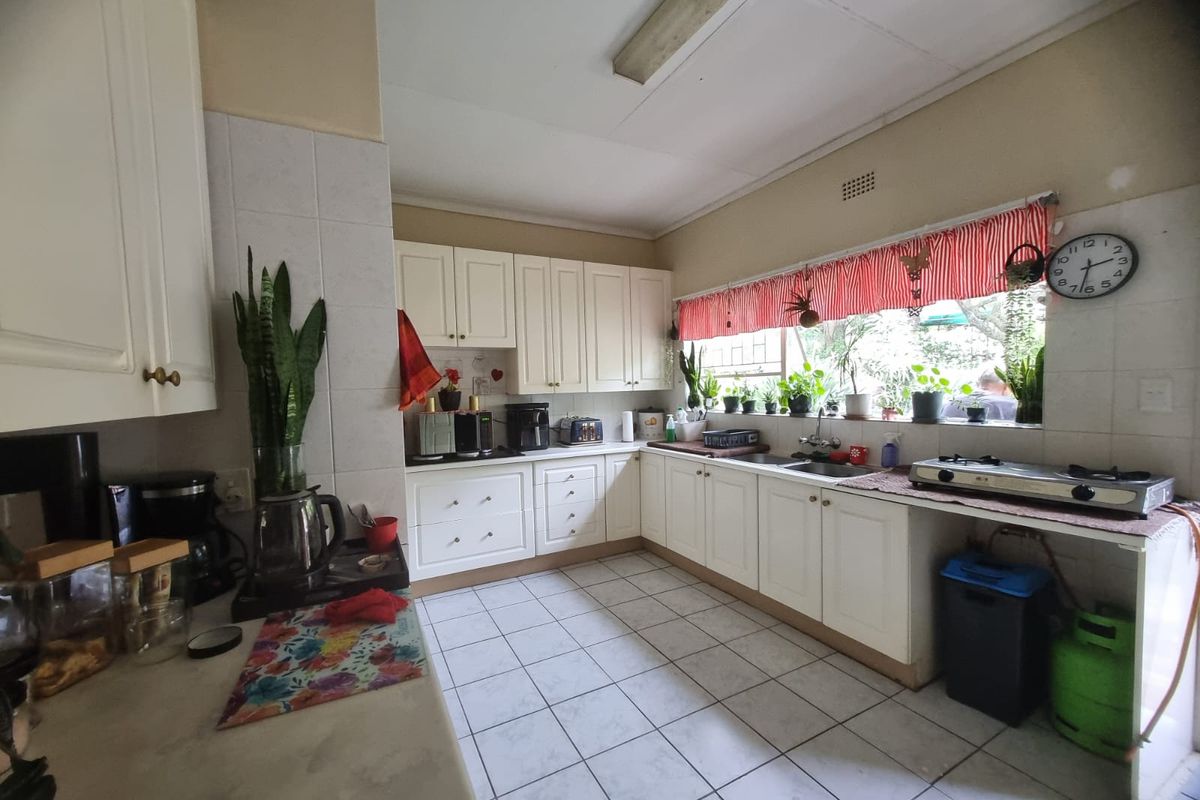 A functional kitchen featuring white built-in cabinetry, tiled flooring, a double basin sink, and a gas hob with ample counter space.