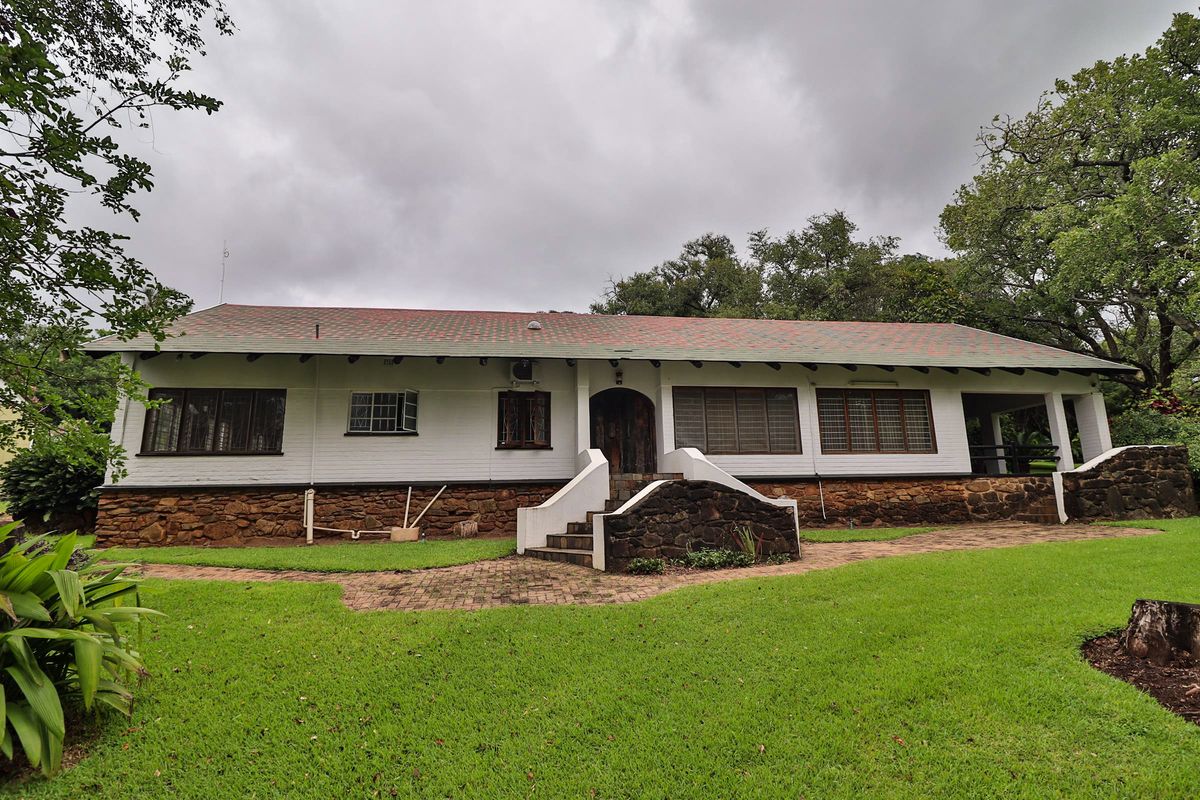 Rear view of a farmhouse featuring a stone masonry base, tiled roof, and a covered patio area set within a spacious garden.