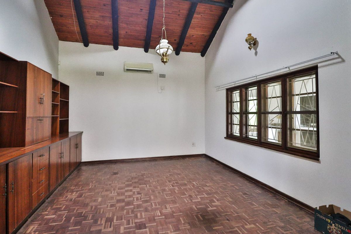 Spacious living area featuring classic parquet flooring, high exposed timber beam ceilings, and extensive built-in wooden cabinetry for storage.