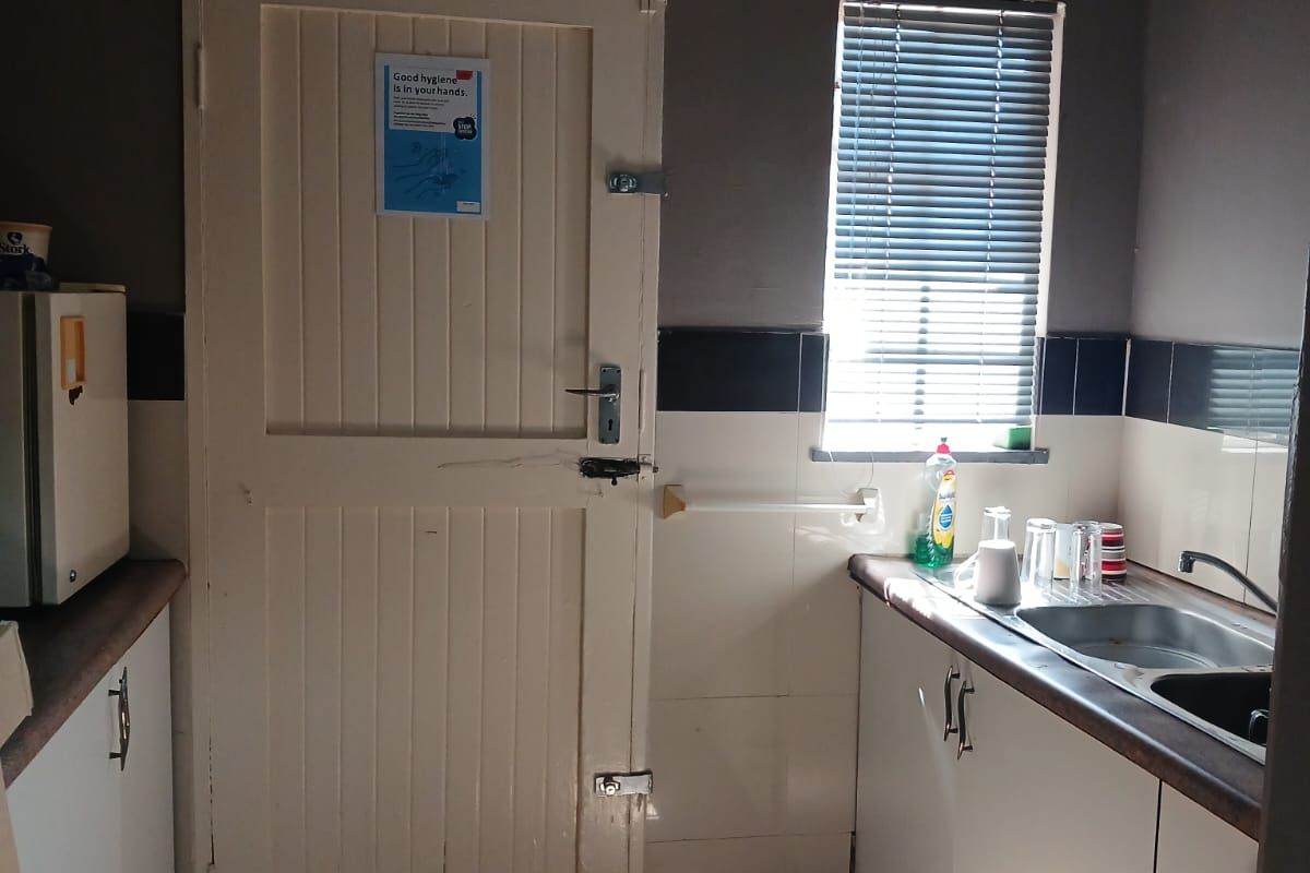A functional kitchen area featuring built-in cabinetry, a stainless steel sink, tiled splashbacks, and tiled flooring, suitable for a compact workspace.