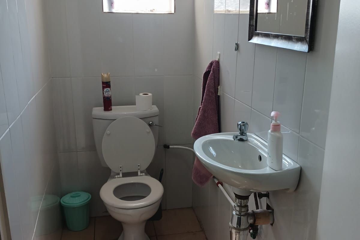 A compact bathroom featuring a wall-mounted basin, standard toilet, and tiled finishes throughout.