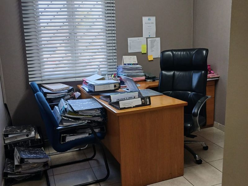 A functional office space featuring tiled flooring, venetian blinds, and a wall-mounted air conditioning unit.
