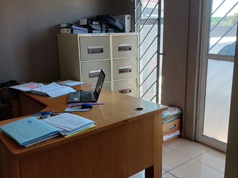 A functional office space featuring tiled flooring, a secure window with burglar bars, and direct access via a glass panel door.