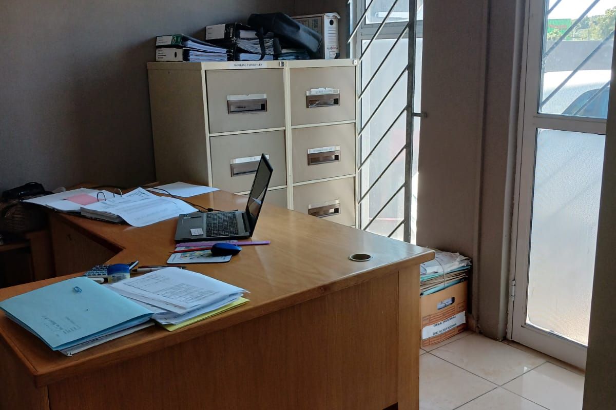 A functional office space featuring tiled flooring, a secure window with burglar bars, and direct access via a glass panel door.