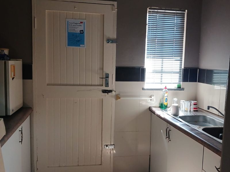 A functional kitchenette featuring built-in cabinetry, a stainless steel sink, tiled splashbacks, and tiled flooring, suitable for office staff use.