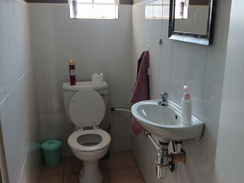 A compact guest bathroom featuring a wall-mounted basin, toilet, and tiled finishes, requiring minor maintenance to the flooring and plumbing fixtures.