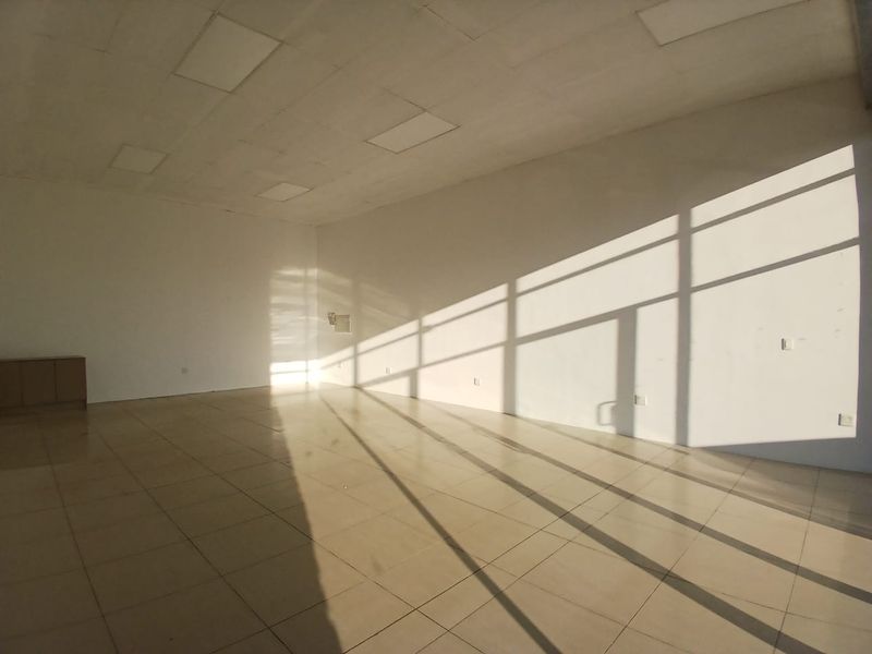 A bright, vacant open-plan retail space featuring tiled flooring, recessed ceiling lighting, and large glass windows allowing for significant natural light.