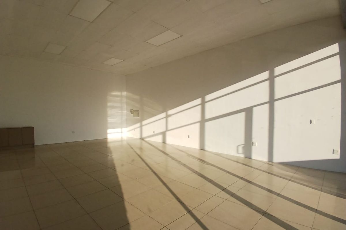 A bright, vacant open-plan retail space featuring tiled flooring, recessed ceiling lighting, and large glass windows allowing for significant natural light.